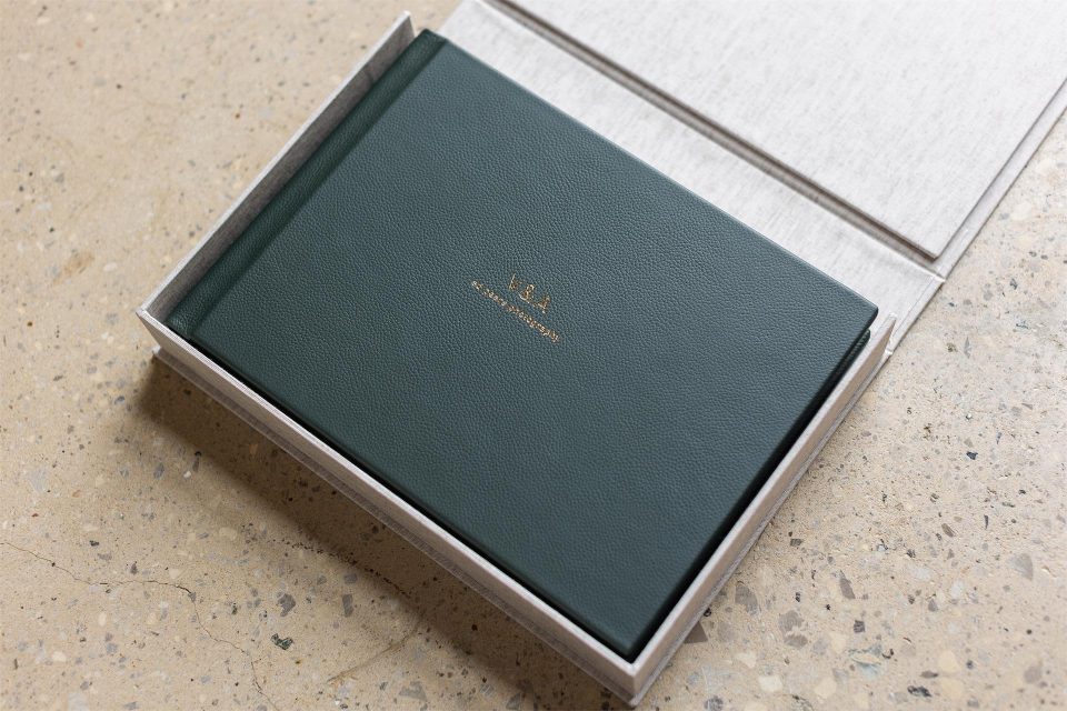 A green leather bound fine art wedding album in a fabric wrapped clamshell box