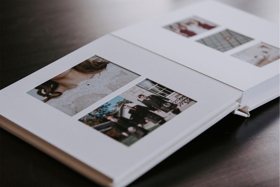 A matted album with wedding photos open on a table showing the bevel cut mounts with images underneath