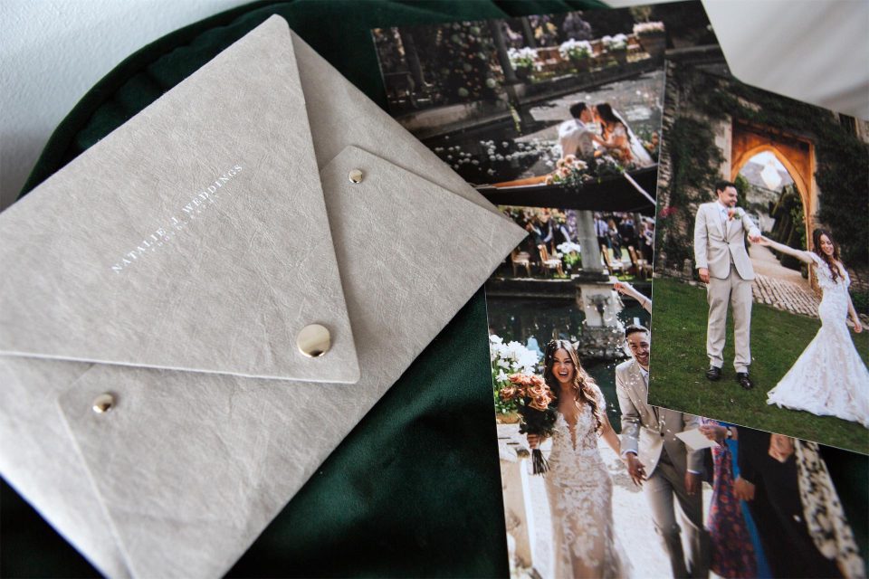 A stone coloured print delivery pouch with white printed personalisation and silver fastenings with a collection of wedding prints