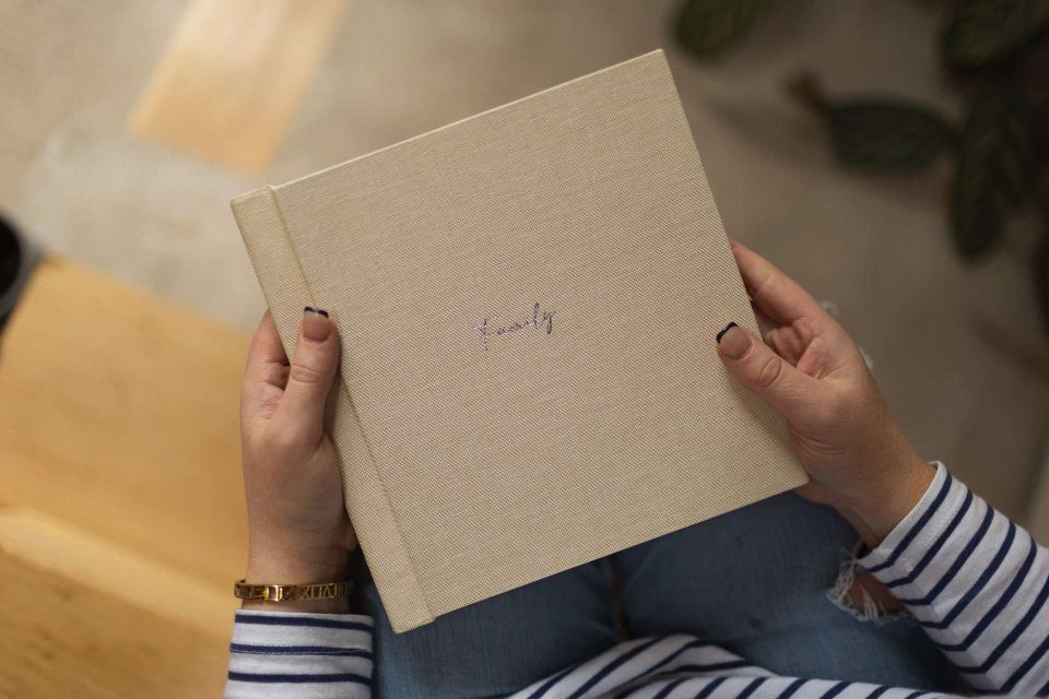 An affordable luxury photo book with silver foiling on the cover and bound in a quality fabric held by a woman