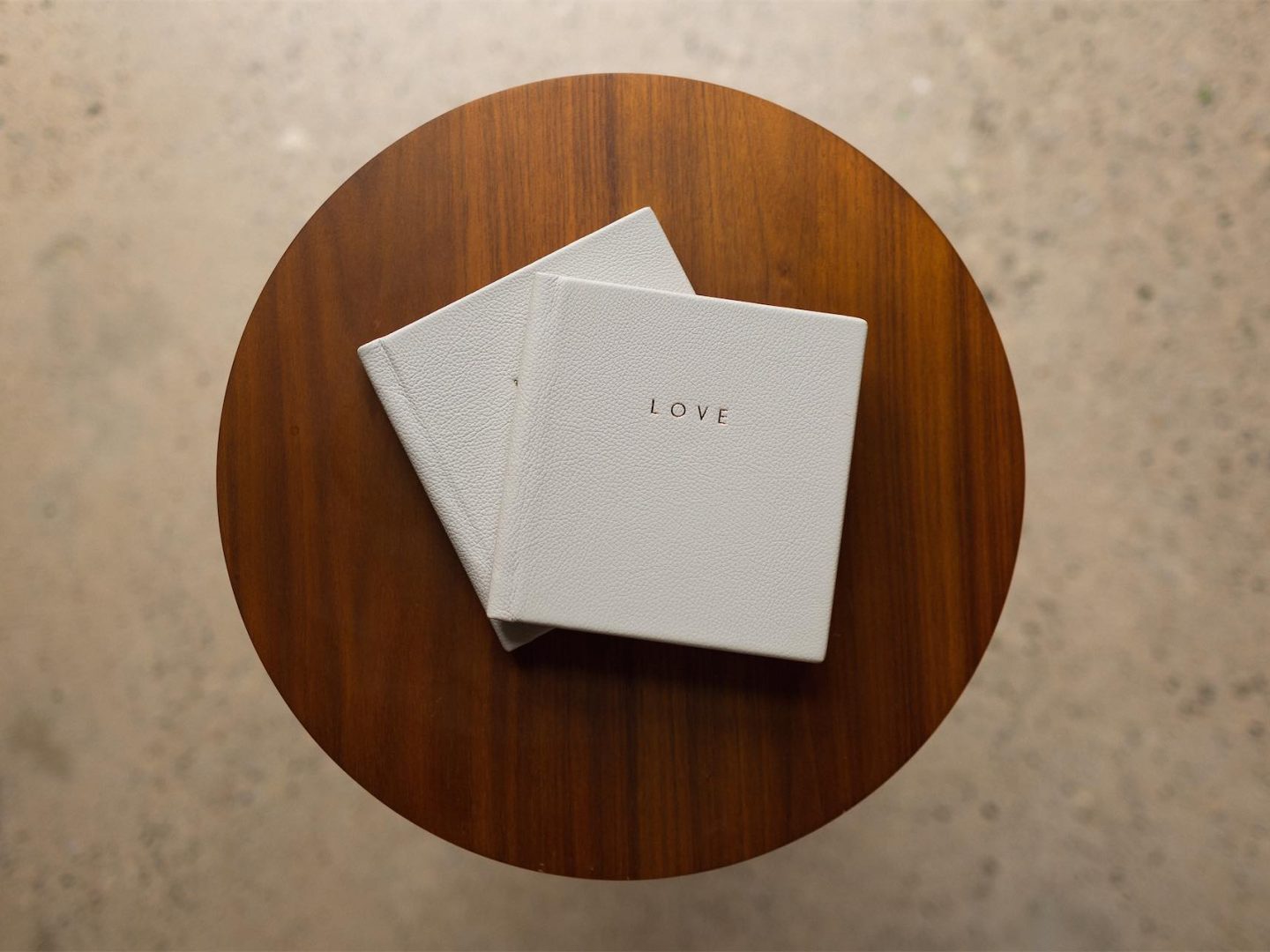 Two smaller copies of a wedding album stacked on a table with the word LOVE gold foiled on the grey leather cover