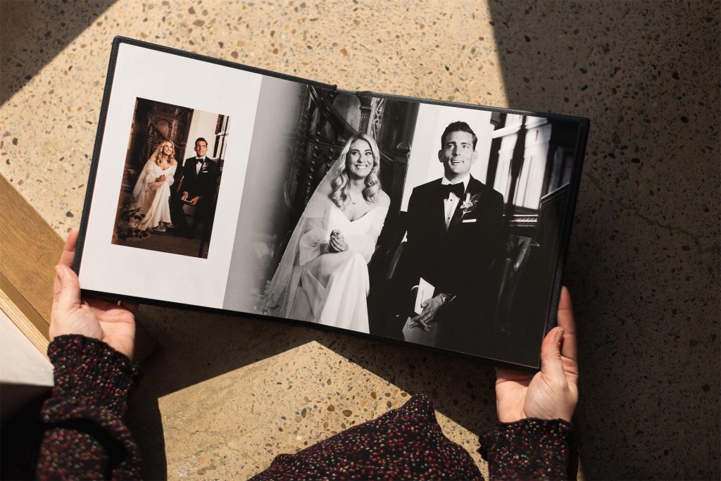 Someone holding open a luxury wedding album with a large black and white photo of a bride and groom in sitting down at church