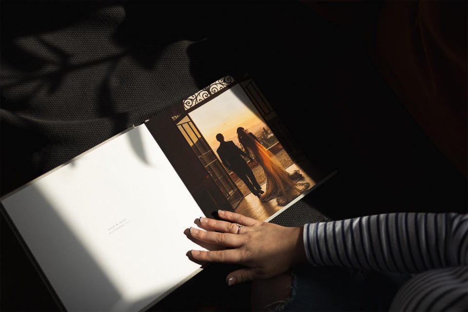 An opened fine art book showing a bride and groom in a doorway and a hand touching the fine art paper.