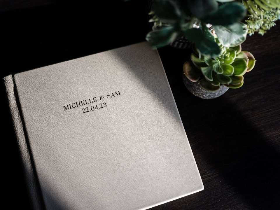 A high contrast image of a leather wedding album on a table with Michelle & Sam text on the cover.