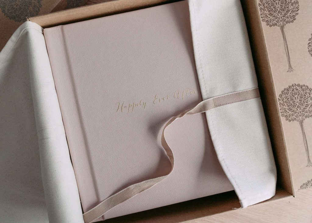 A blush pink luxury album with real gold cover text in a natural cotton wrap and ribbon