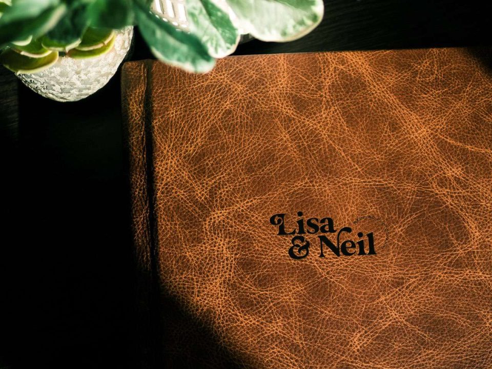 Lisa & Neil studio sample wedding album in saddle leather pictures next to some plants.