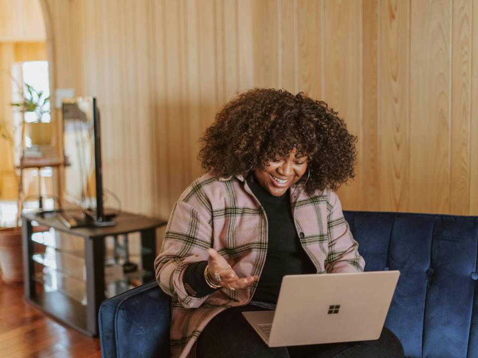 A lady siting on a sofa with a laptop on her lap and having a Zoom call