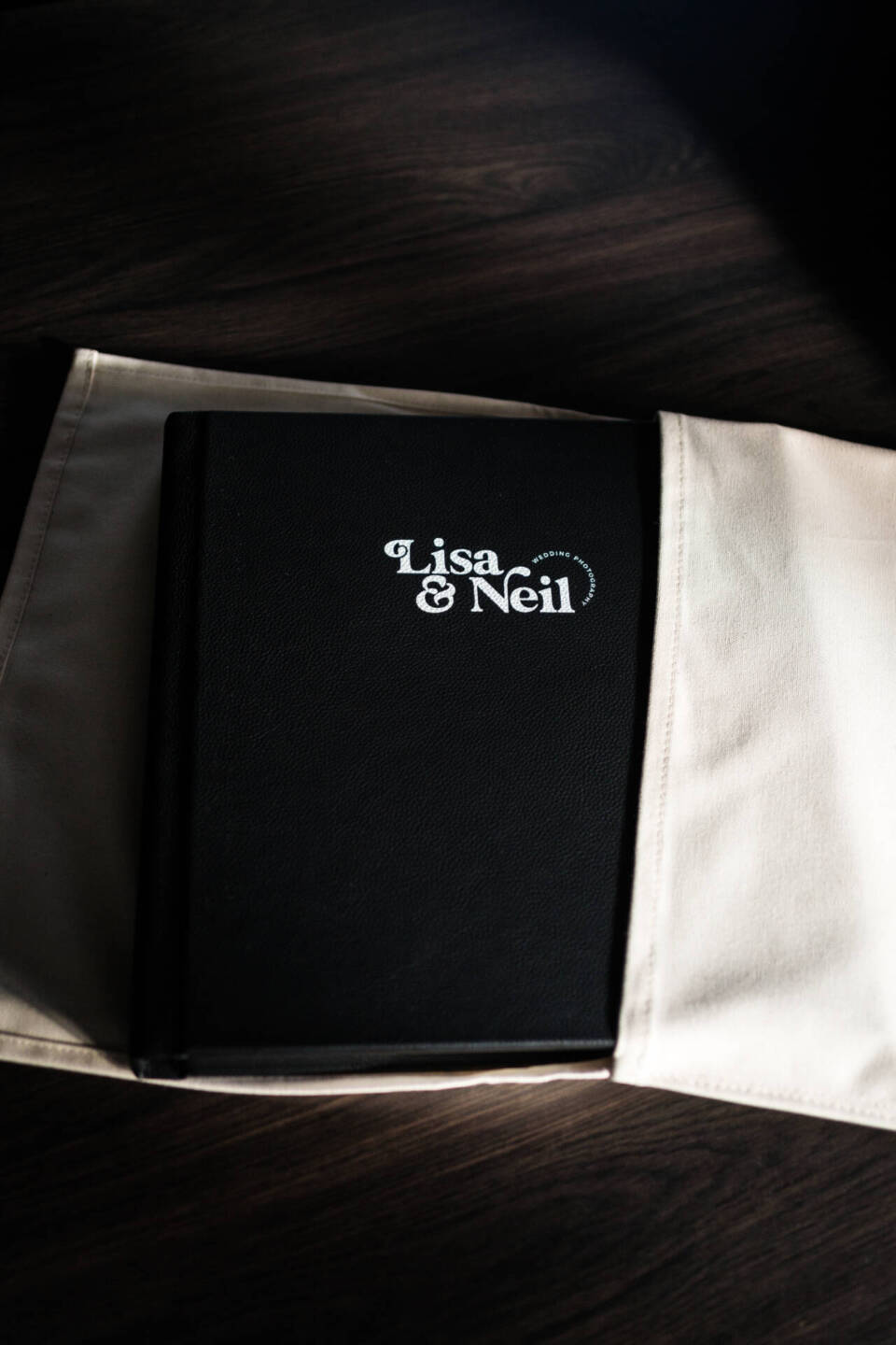 A black leather photo album being removed from its natural cotton bag with white cover personalisation with a photographer's studio logo