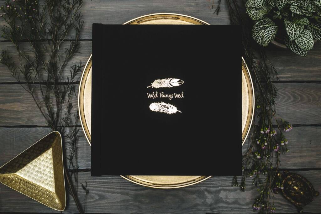 a black foiled photo album on a gold plate surrounded by plants