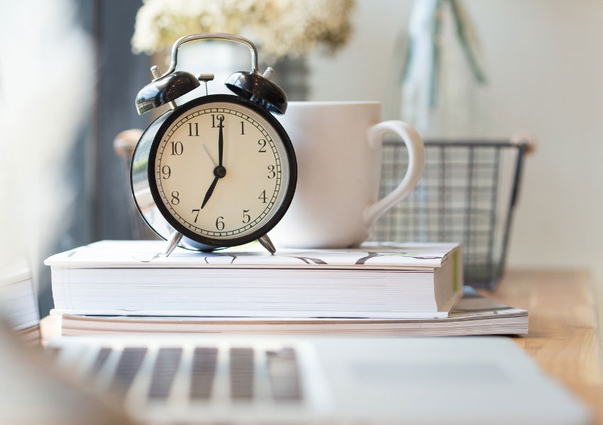 black clock on a desk next to a laptop 