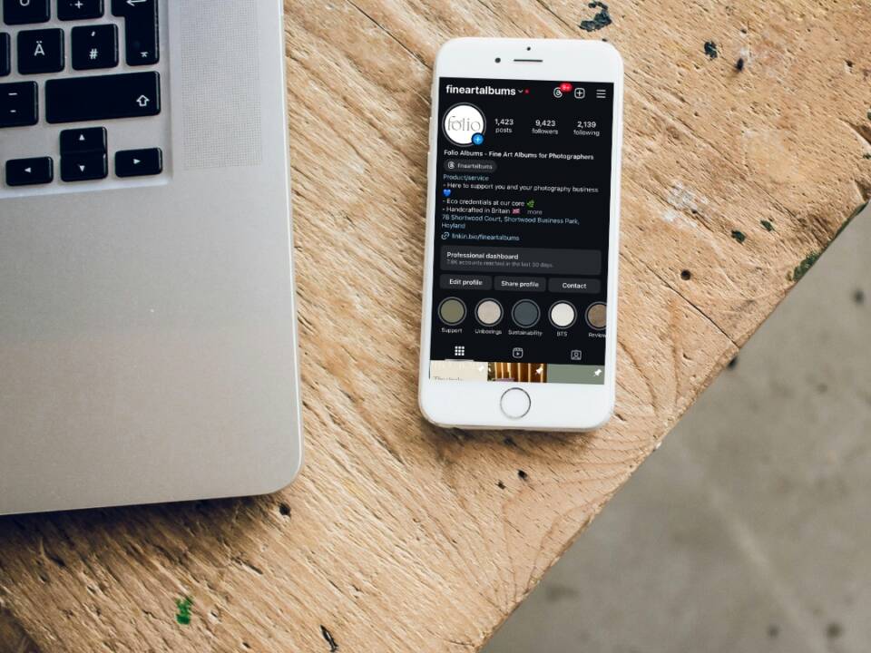 phone on table next to laptop showing Instagram page of album supplier Folio Albums