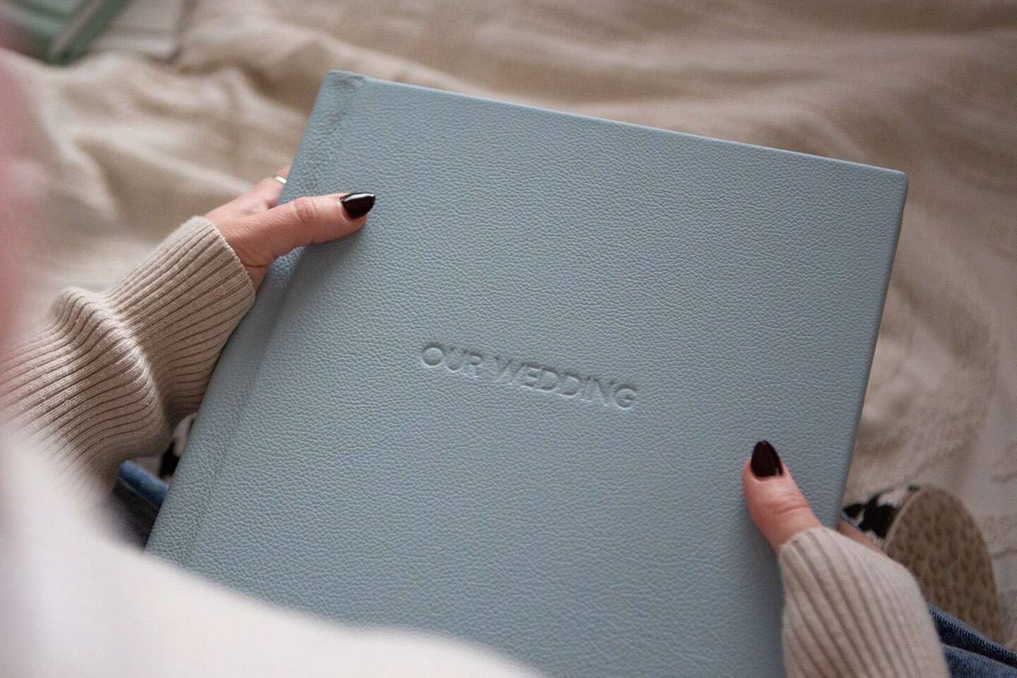 Hands holding a blue Luxe Album with Our Wedding blind debossed on the front