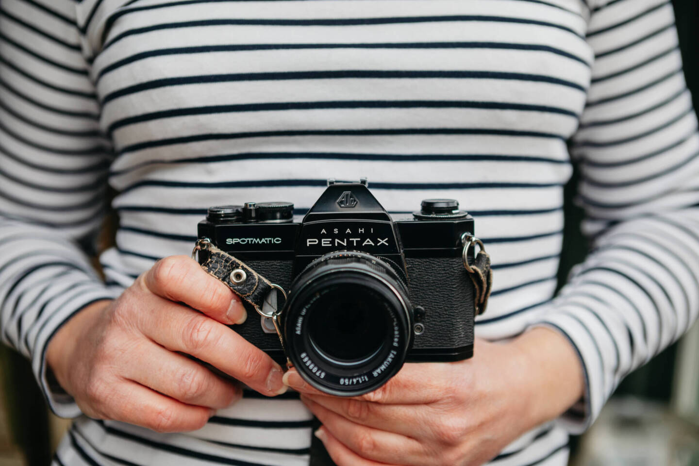 woman in striped top holding an old Pentax spotmatic camera used to take photographs 