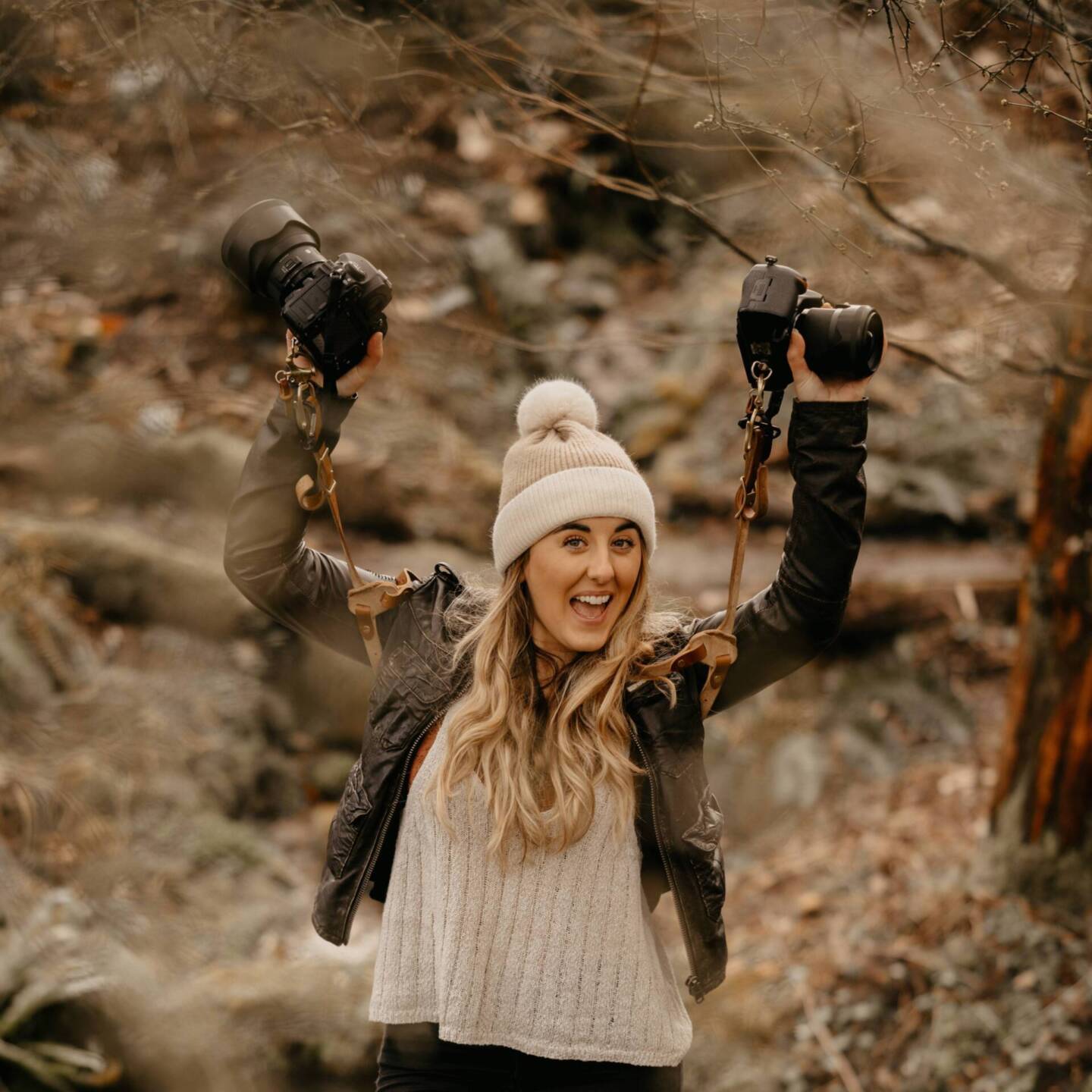 Female photographer holding up cameras in a wood 