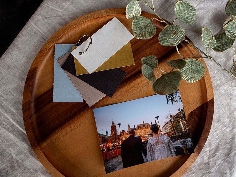 wedding image prints on a wooden board next to silk material swatches and foliage 