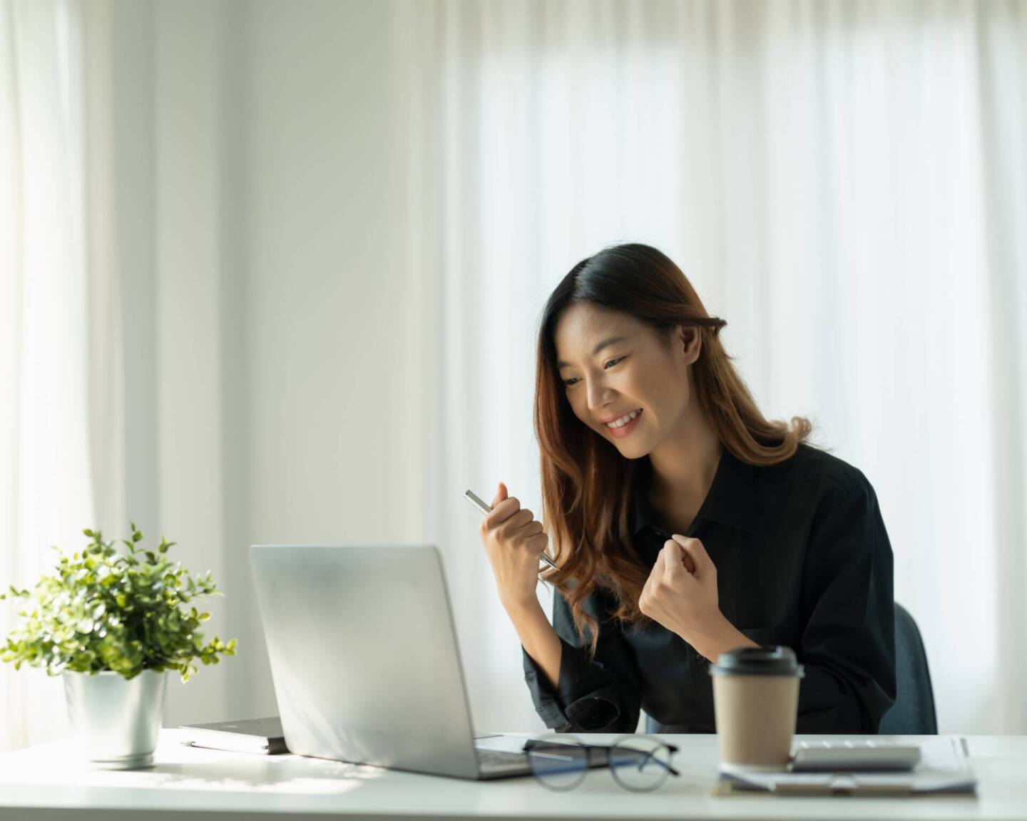 woman looking at laptop on her desk cheering