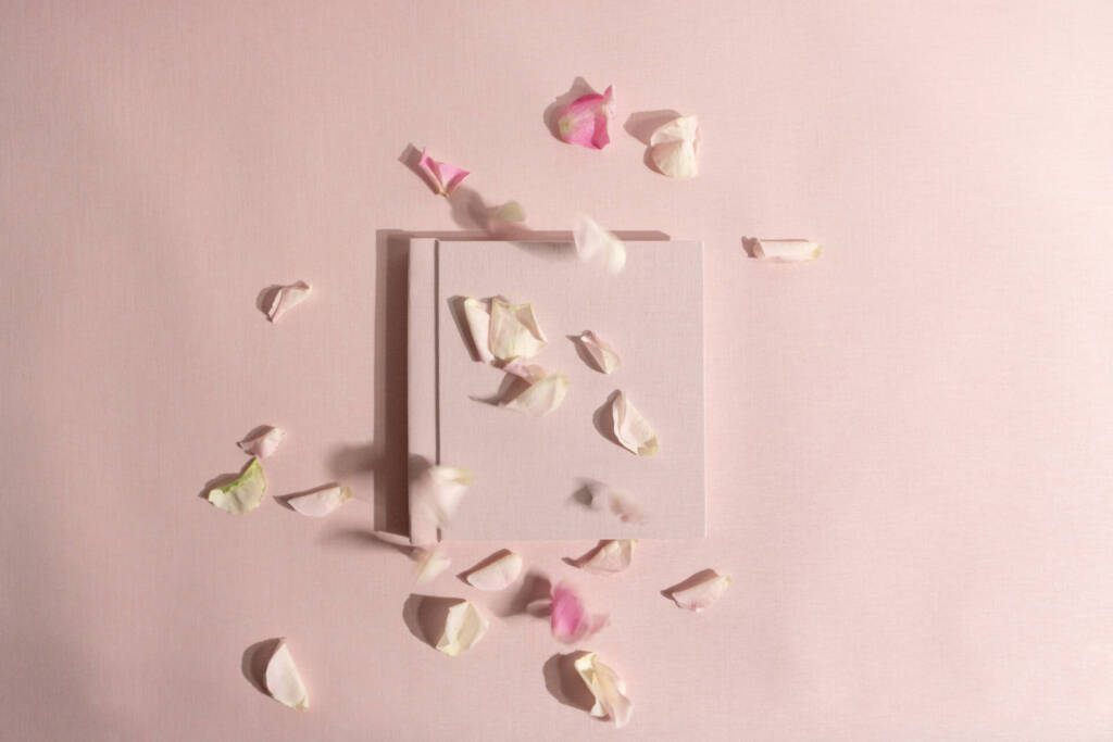 a pink photo album on a pink background with rose petals covering it