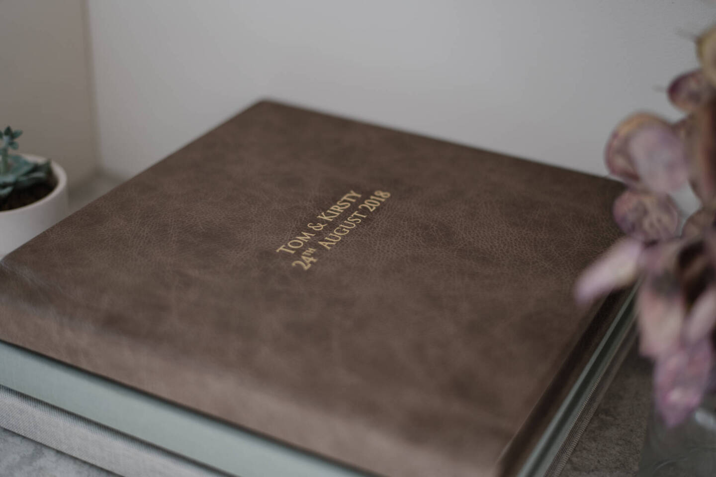 wedding album stacked on a shelf next to flowers 