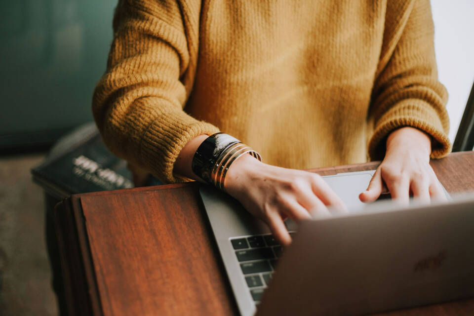 Woman in yellow jumping using laptop to search for album supplier.