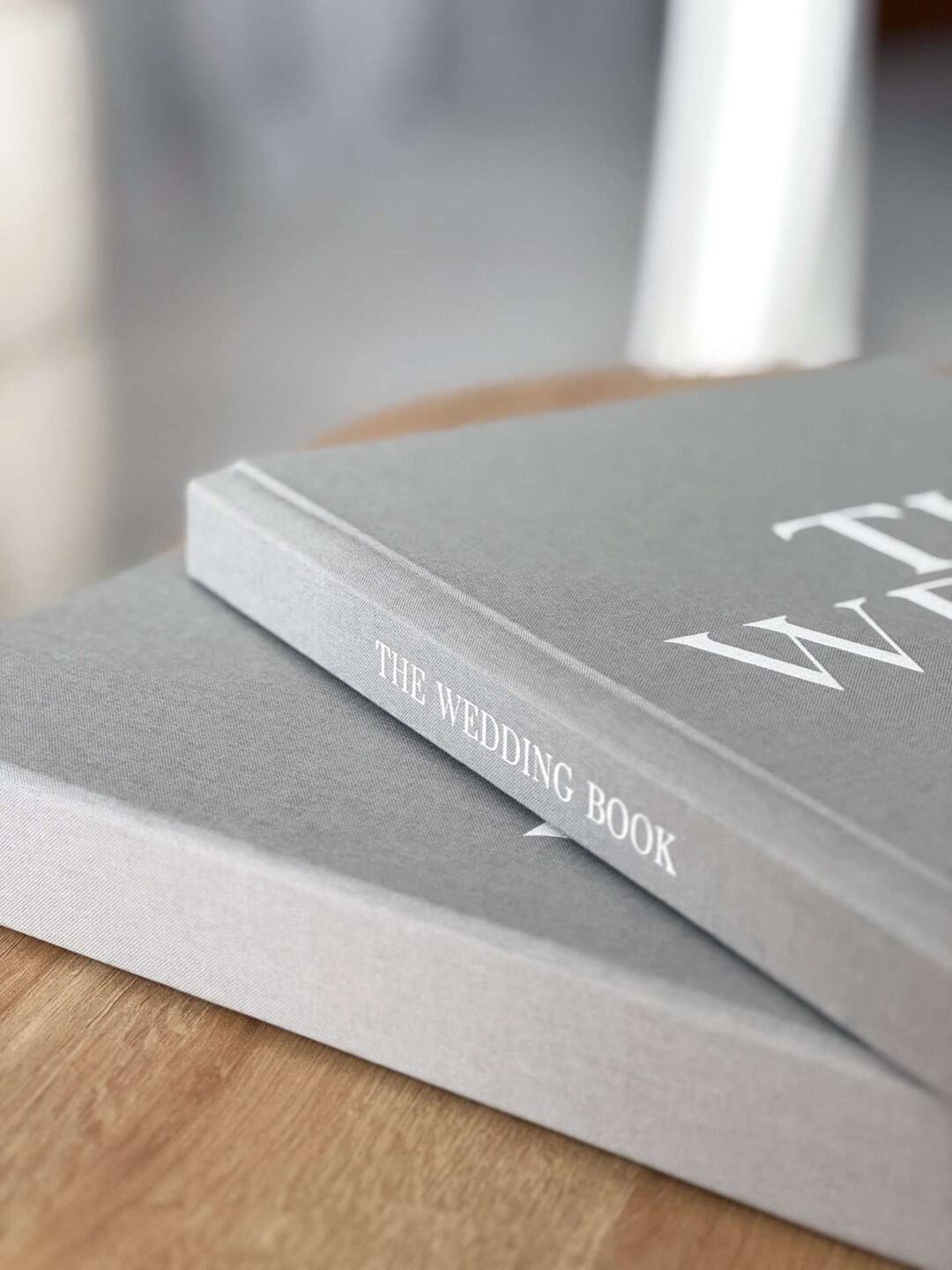 A close up image of a grey fabric Coffee Table Book with white cover printing spine personalisation on a wooden table.