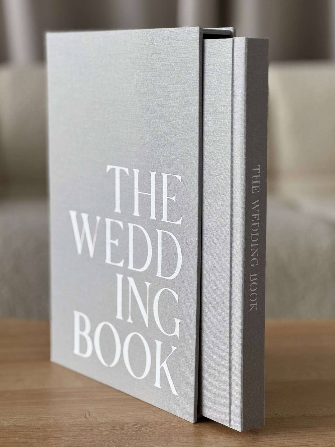 A grey Coffee Table Book in a slipcase with white cover printing personalisation stood up on a wooden coffee table.