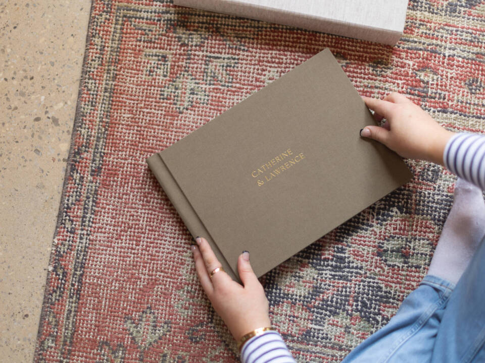 a green wedding photo album in a woman's hands sat on a patterned rug