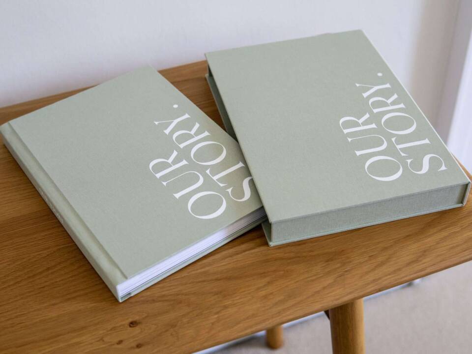 A pistachio coloured slipcase and coffee table photo book on a wooden table