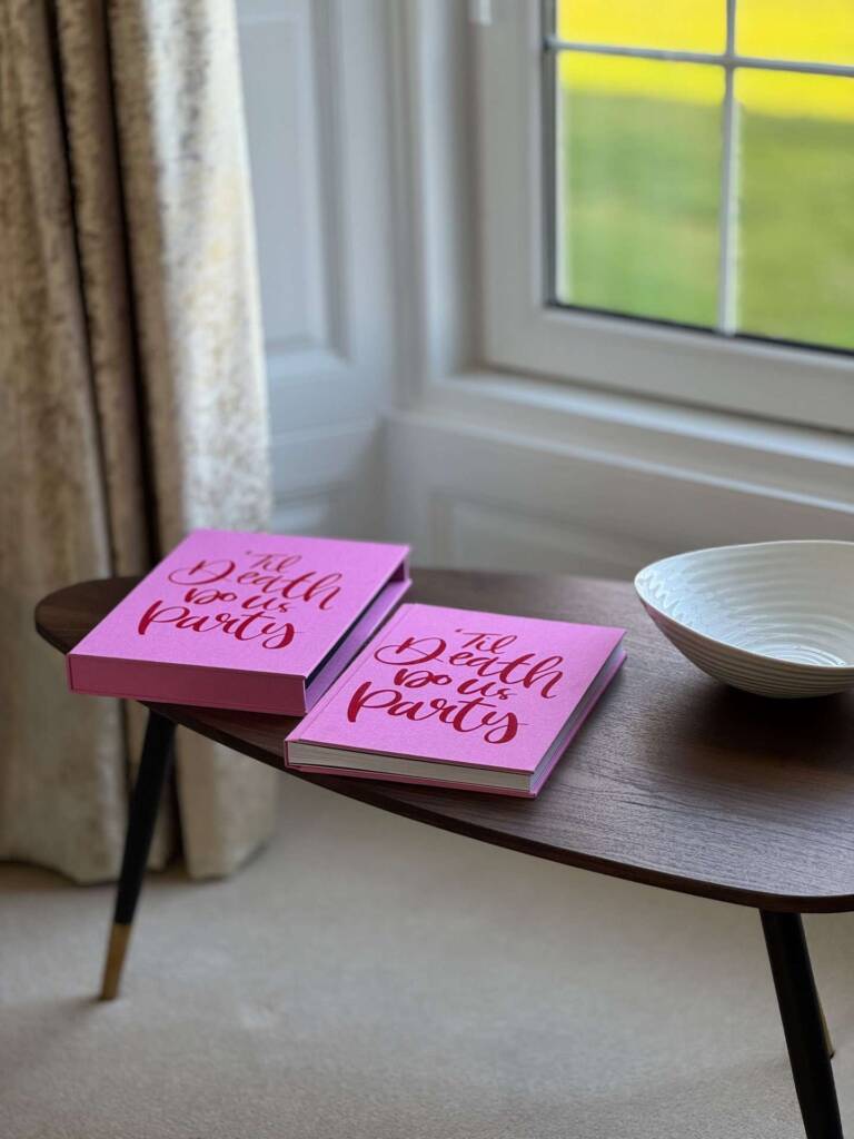 A pink fabric called Rhubarb coffee table book with slipcase on a table in front of a window