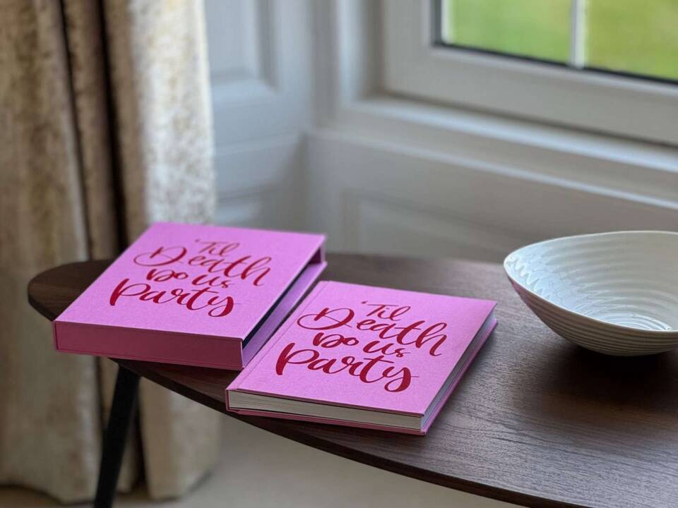 A pink fabric called Rhubarb coffee table book with slipcase on a table in front of a window
