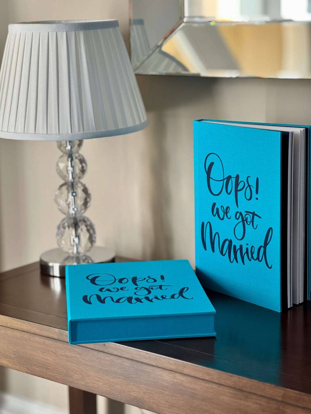 A blue coffee table photo book next to its slipcase with Oops! We Got Married text in blue ink on the cover