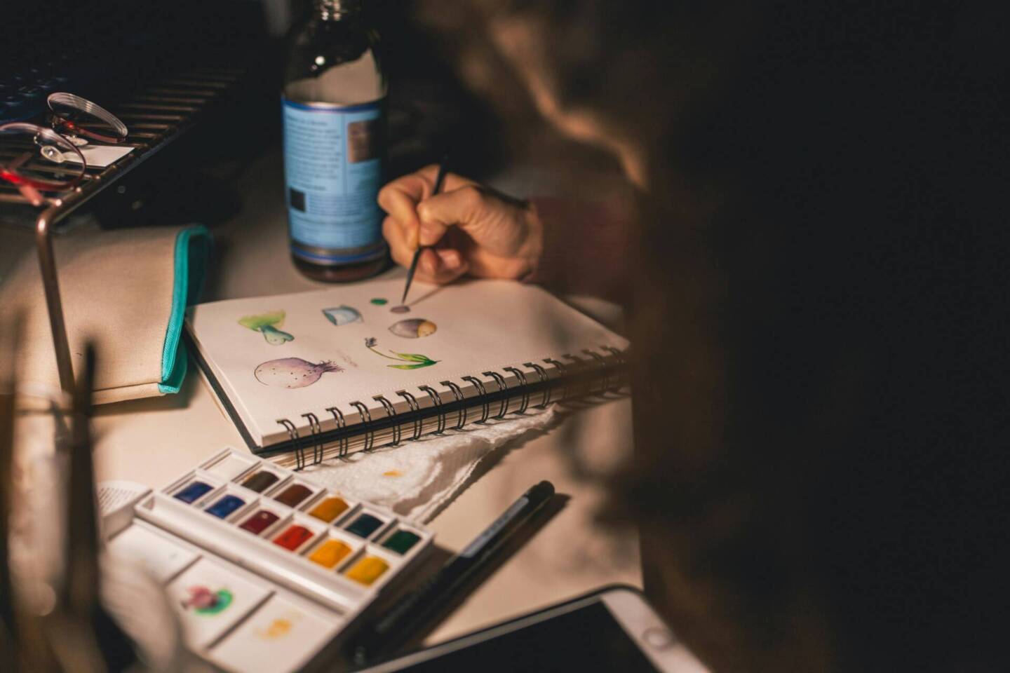 person colour painting on a desk notepad in the dim lighting