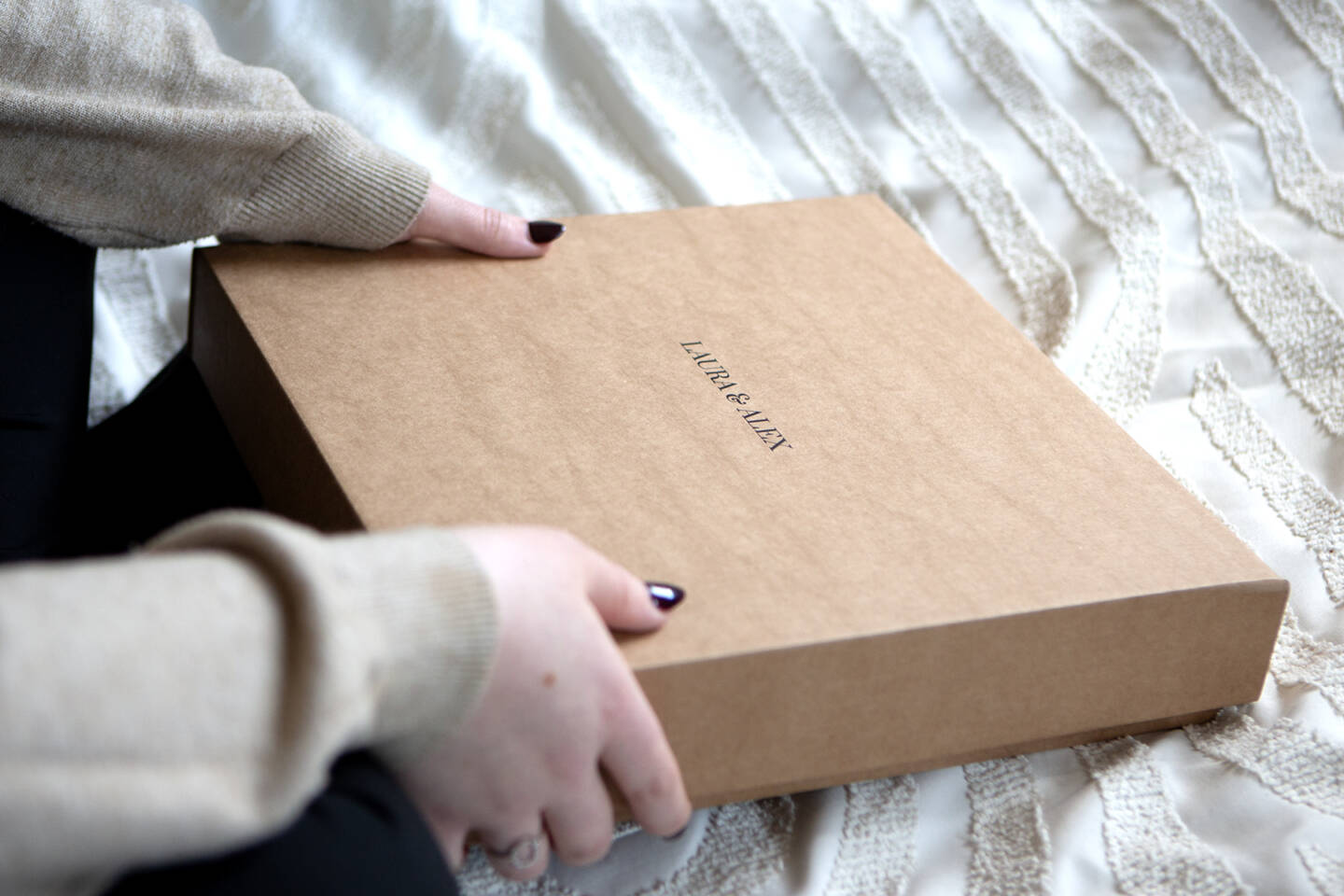 A bride opening her wedding anniversary gift a wedding album featuring wedding photography with the names Laura & Alex in black printing