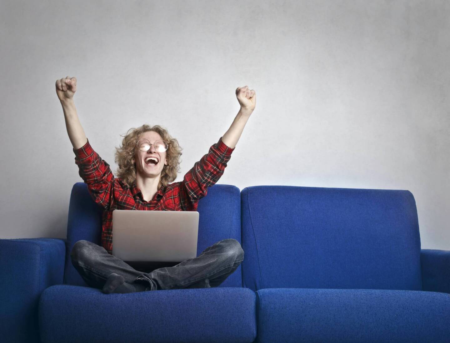 woman sat of blue sofa with laptop on lap cheering