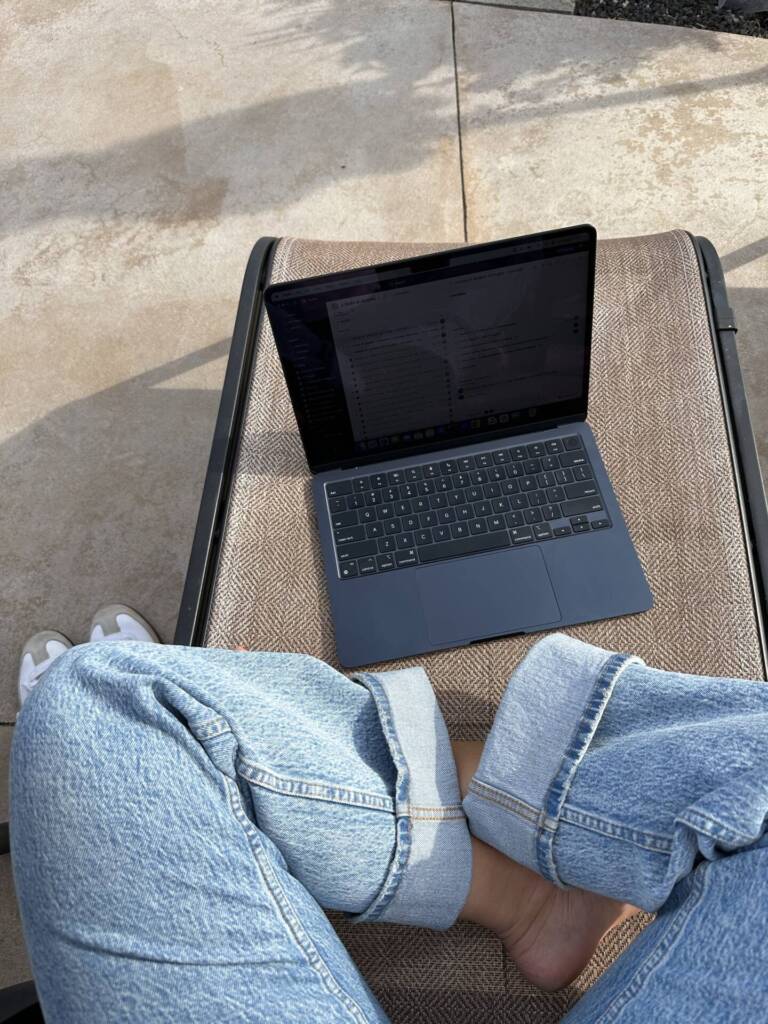 a photographer working on her laptop working with photography clients. She is wearing jeans and is crosslegged.